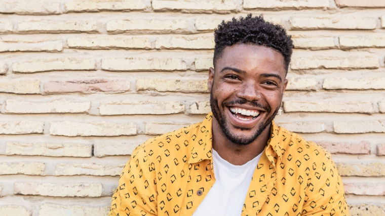 The-Life-Changing-Benefits-of-Combining-Medication-and-Therapy Smiling black man standing in front of a beige brick wall | The Life-Changing Benefits of Combining Medication and Therapy | Mindful Health Solutions