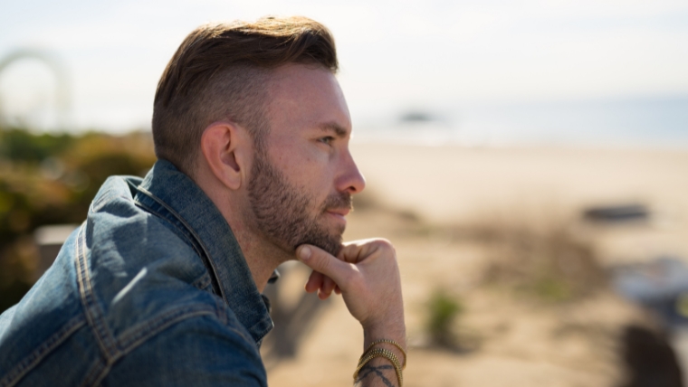 Bipolar Disorder and Bipolar Cycles: What you need to know | Mindful Health Solutions White man at the beach with his hand on his chin thinking | Bipolar Disorder and Bipolar Cycles: What you need to know | Mindful Health Solutions