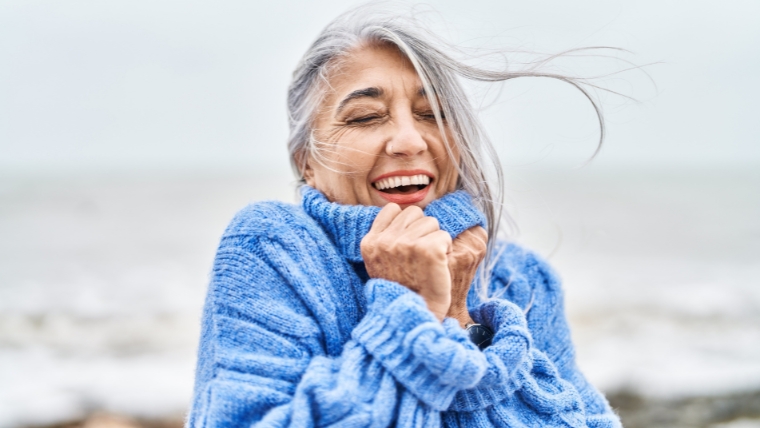 Is-Esketamine-Nasal-Spray-Safe-and-Effective-for-Depression-In-Elderly-Patients Older woman with white hair in an oversized blue sweater on the beach with eyes closed and a smile | Is Esketamine Nasal Spray Safe and Effective for Depression In Elderly Patients | Mindful Health Solutions