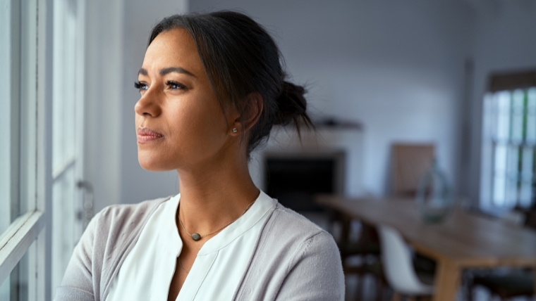 Thoughtful woman of color looking outside window | Are You Skeptical About TMS Discover What the Science Is Saying | Mindful Health Solutions