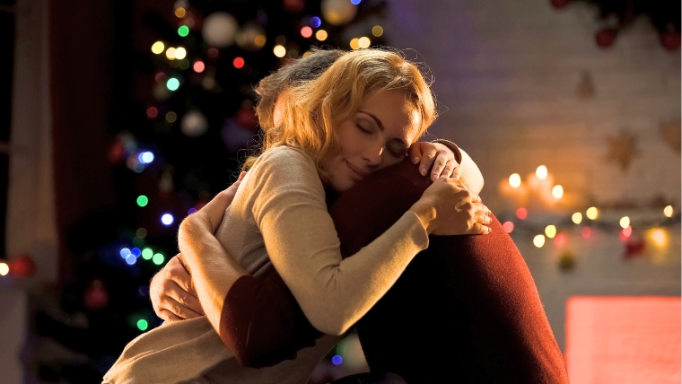 A man and woman hugging in front of a Christmas tree | How To Support Loved Ones with Mental Health Challenges During the Holidays | Mindful Health Solutions