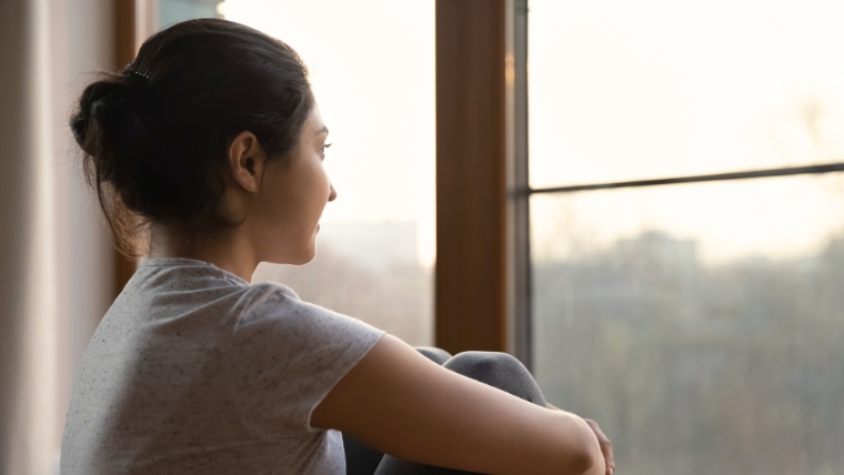 Could-TMS-Help-You-Explore-This-Science-Backed-Revolution-in-Mental-Health Woman hugging her knees while looking out the window with a hopeful look on her face | Could TMS Help You Explore This Science-Backed Revolution in Mental Health | Mindful Health Solutions